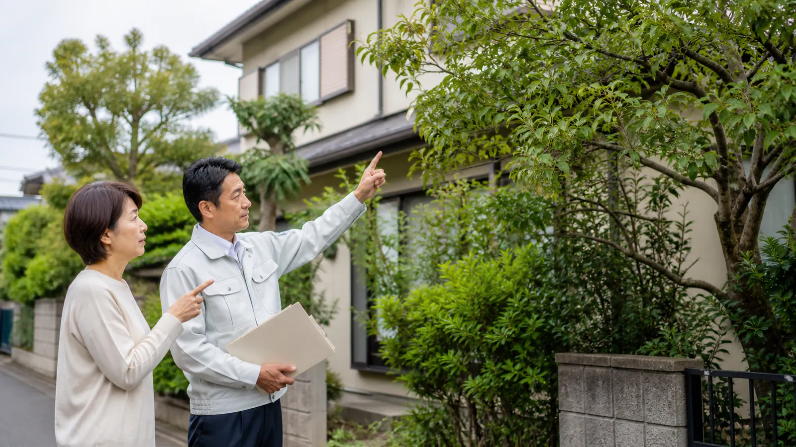 空き家の道路側へ伸びた庭木と境界を確認する家族と庭管理担当者